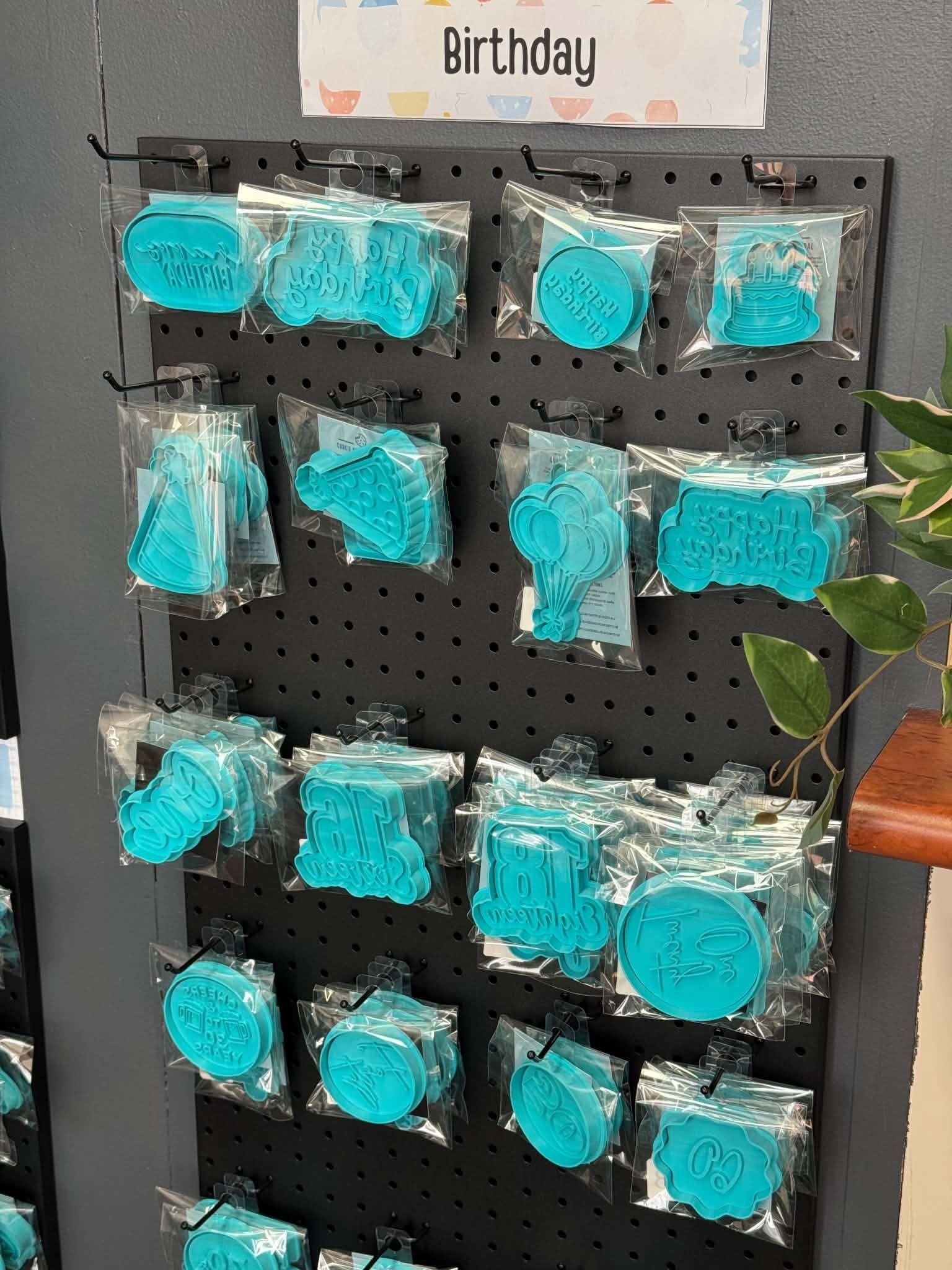 Packaged turquoise birthday cookie cutters and stamps hanging on a display
